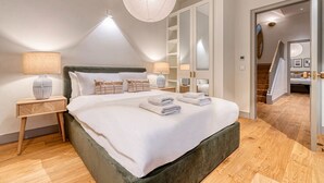 Een slaapkamer met een groot bed, twee nachtkastjes, een hanglamp en een kledingkast.