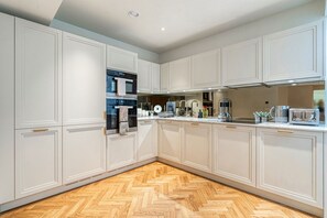 A modern kitchen with white cabinetry, a herringbone wood floor, and stainless steel appliances. - Westminster Fire Station Chic Apartments (London)