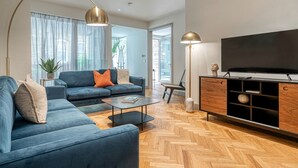 Een moderne woonkamer met een zithoek, een salontafel, een televisie en een houten visgraatvloer.