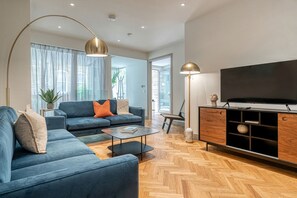 A modern living room with a sofa set, a coffee table, a TV, and a wooden herringbone floor. - Westminster Fire Station Chic Apartments (London)