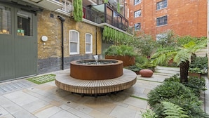 Une cour avec un banc circulaire en bois, un foyer et des plantes en pot.