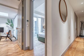 Ein modernes Hotelzimmer mit Holzboden, einem großen Spiegel und Blick auf die Stadt durch raumhohe Fenster.