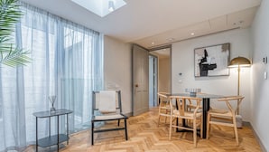 Un salon moderne avec un parquet en chevrons, une table basse en verre, un canapé noir et un coin repas comprenant une table et des chaises en bois.