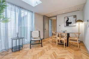 Ein modernes Wohnzimmer mit Fischgrätparkett, einem Glastisch, einer schwarzen Couch und einem Essbereich mit Holztisch und Stühlen.