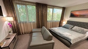 A hotel room with a bed, a sofa, a desk with a lamp, and a window with curtains.