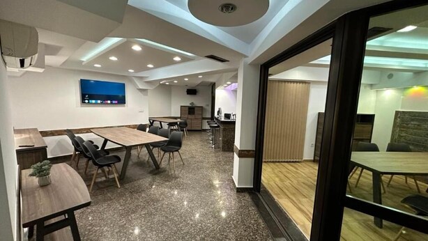 A modern conference room with a large table, chairs, a TV screen, and a ceiling with recessed lighting.