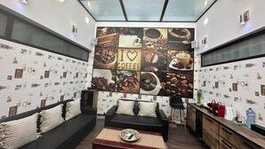A modern room with a large coffee-themed wall mural, a sofa, a small table, and a kitchen area with a water dispenser.