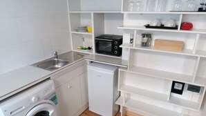 Cuina compacta amb rentadora, rentavaixelles, microones i armaris blancs.