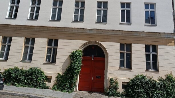 Un edifici de diversos pisos amb una porta vermella, nombroses finestres i una entrada ben visible.
