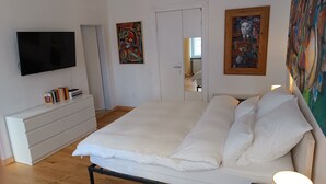Un dormitori amb un llit, una televisió, una petarrera i quadres a les parets.