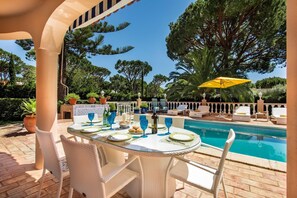 An outdoor dining area with a pool, white wicker chairs, and a yellow umbrella. - Villa Daniela Quarteira (Quarteira)