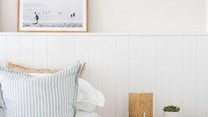 A neatly made bed with striped pillows, a framed picture on the wall, a small wooden nightstand with a lamp and a plant, and a white headboard. - Rosebud’s Modern Coastal Escape • Walk to Beach • Sleeps 10 (Rosebud)