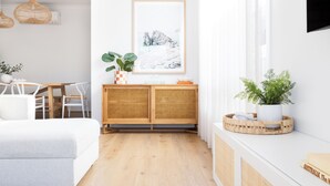 A modern living room with a sofa, a dining table, and a wooden cabinet with plants. - Rosebud’s Modern Coastal Escape • Walk to Beach • Sleeps 10 (Rosebud)