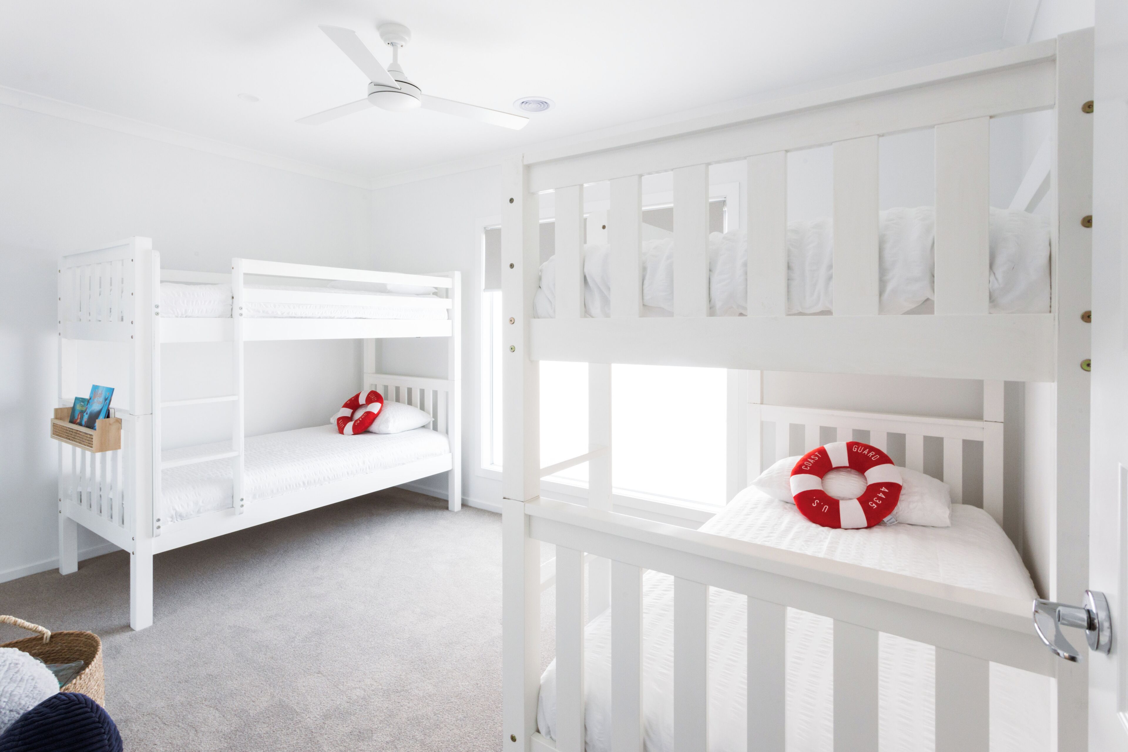 Una habitación blanca con literas, un ventilador de techo y una puerta blanca.