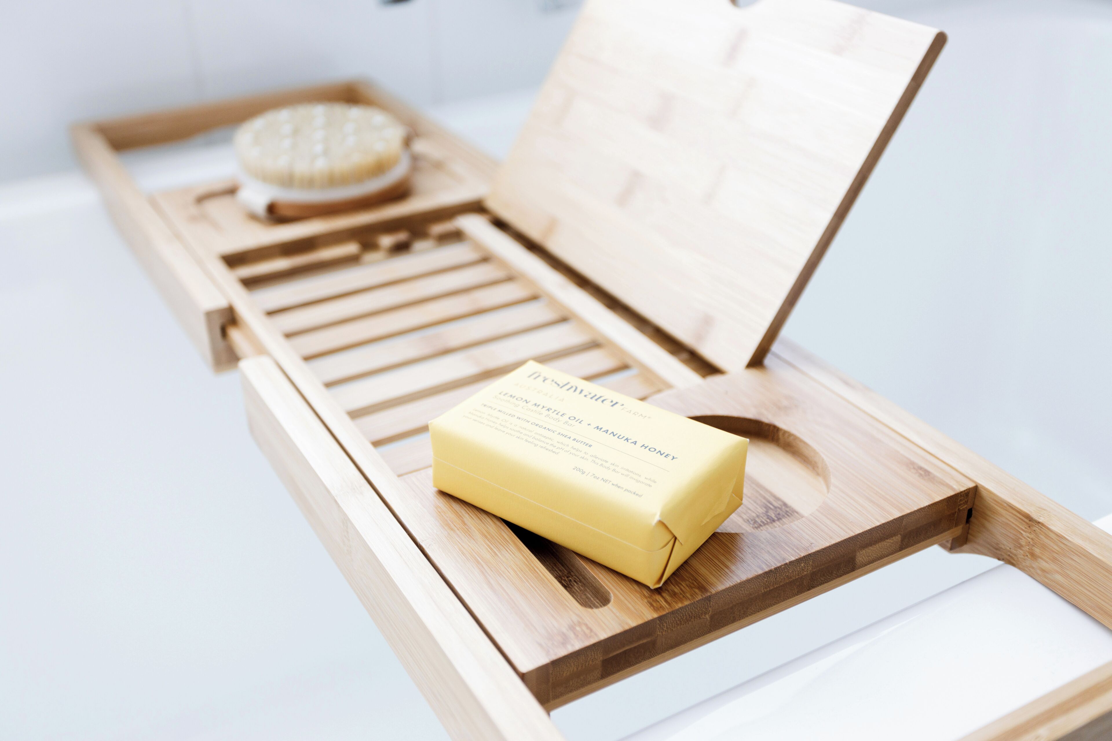 Un plateau en bois sur lequel se trouvent un savon et un récipient rond, vraisemblablement une boule de bain effervescente, le tout posé sur une surface blanche.