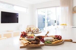 Una habitación bien iluminada con una gran mesa de comedor dispuesta para una comida, mostrando varios quesos, frutas y galletas.