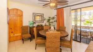 A dining area with wicker chairs, a round table, a ceiling fan, and a view through a glass door. - 2BD Condo in La Costa Phase 2! (San Jose del Cabo)