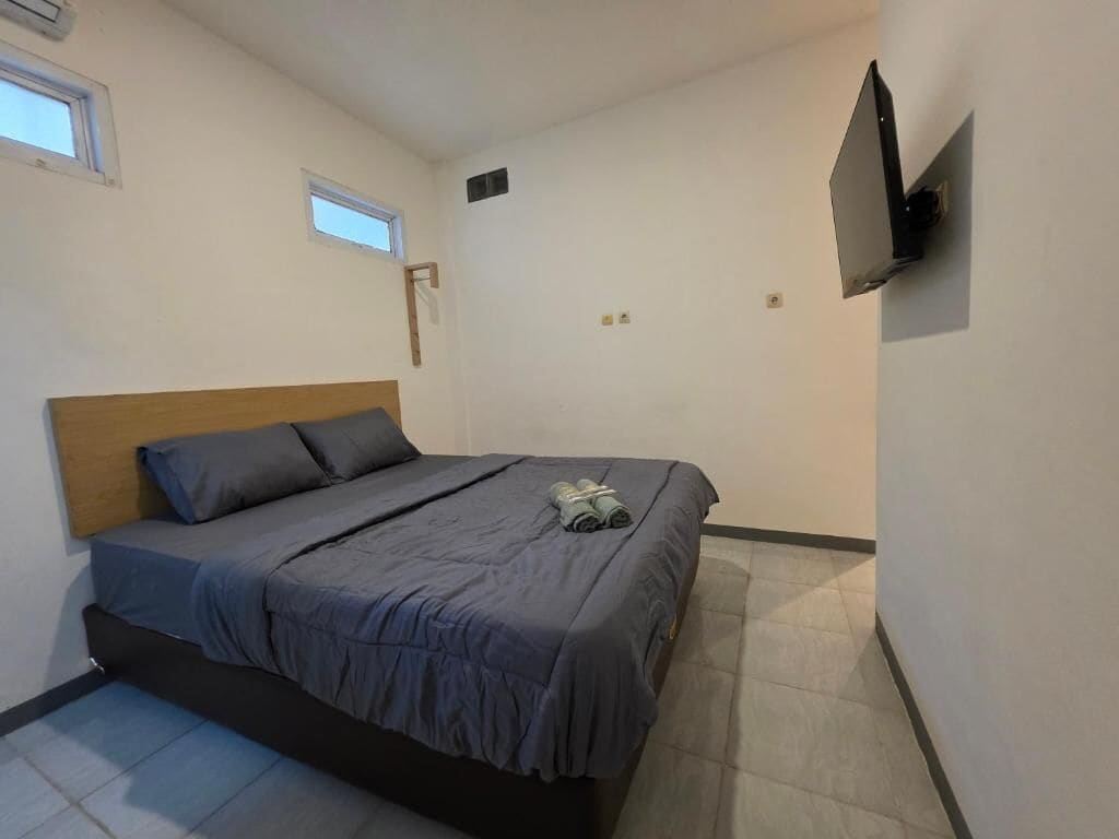 A bedroom with a single bed, a flat-screen TV mounted on the wall, and a small window.