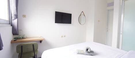 Una habitación de hotel con cama, un escritorio con silla, un televisor montado en la pared y una puerta.