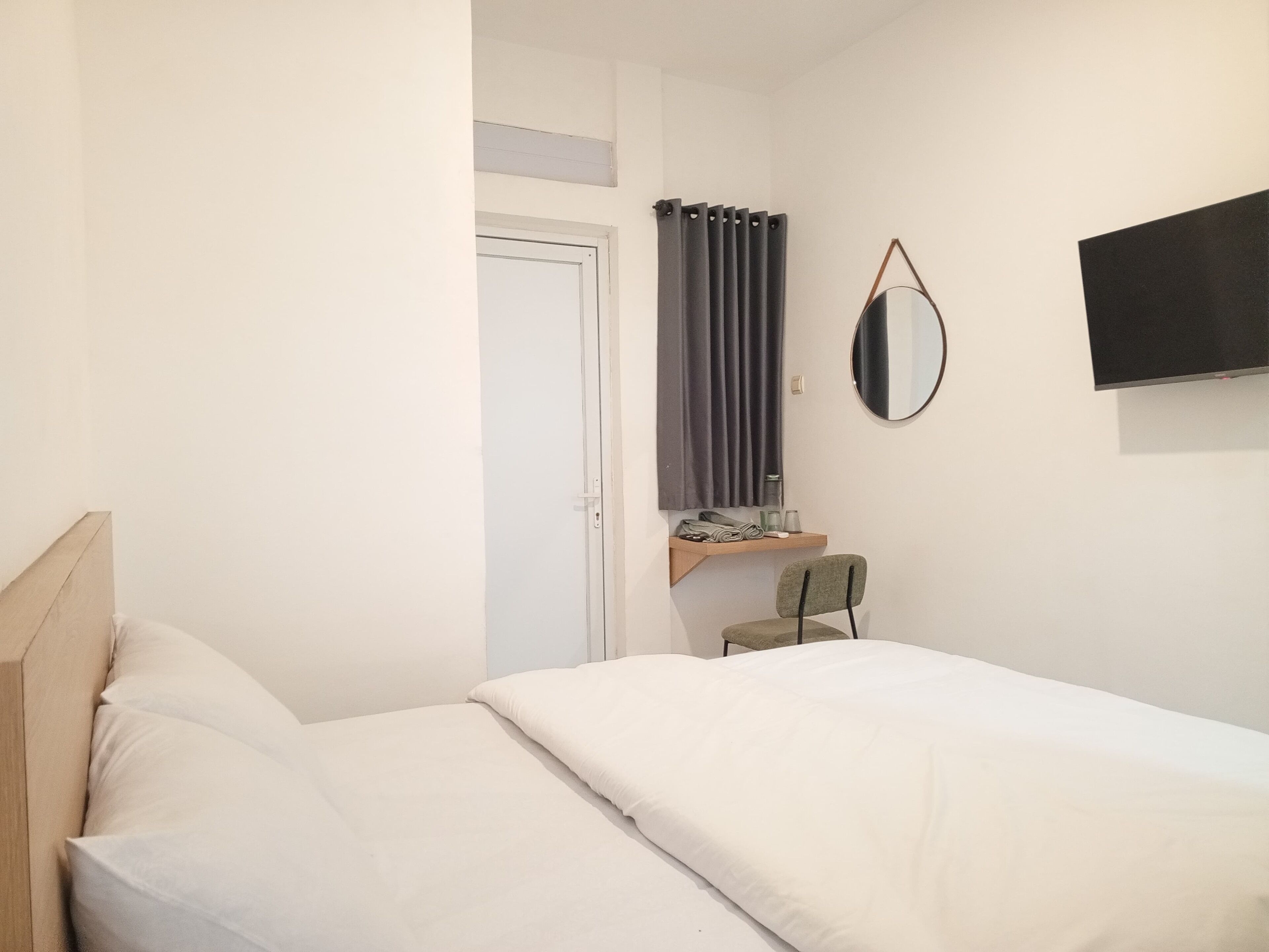 Ein Schlafzimmer mit einem Bett, einem Sessel, einem Fernseher, einem Spiegel und einer Tür.