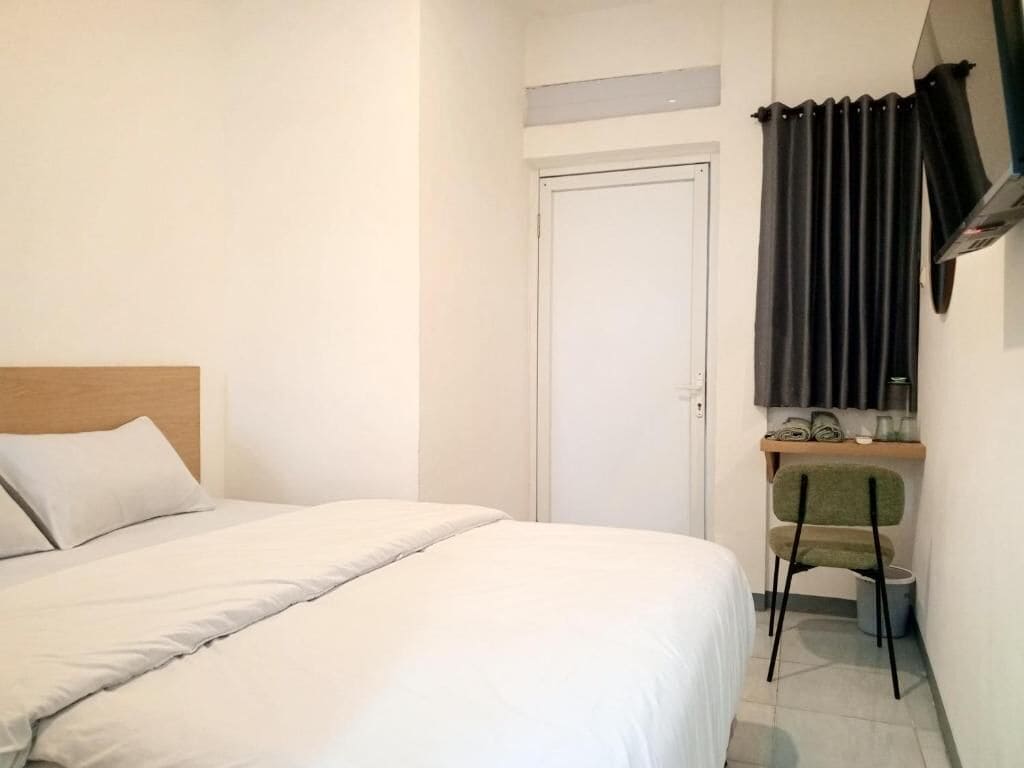 Une chambre à coucher avec un lit, une chaise, un bureau, une porte et une fenêtre avec des rideaux.