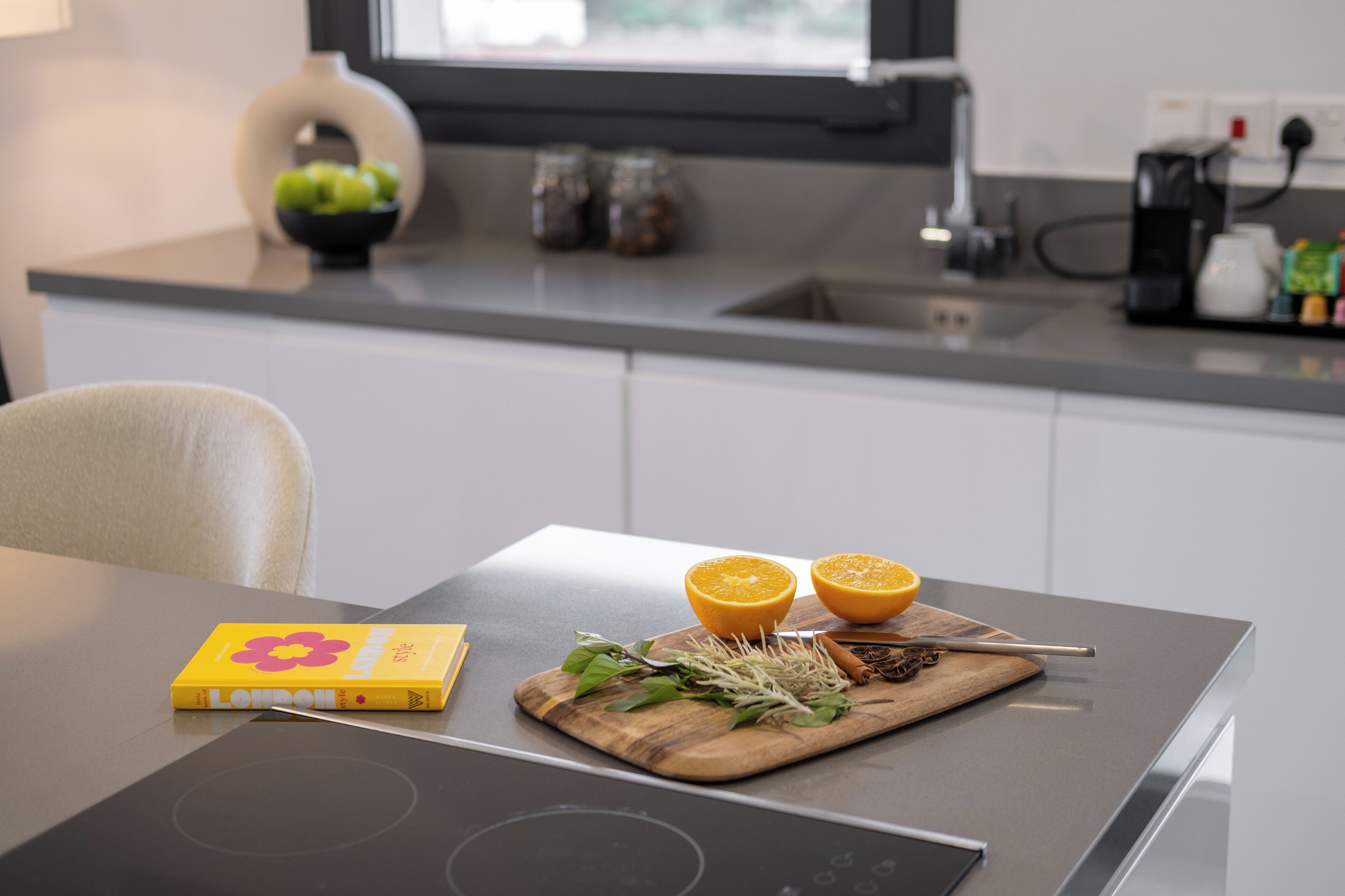 A modern kitchen with a cutting board, fresh herbs, and a book on the counter.