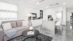 A modern living room with a sofa, a coffee table, and a kitchen area with a bar. - Noir Luxury Residence - Rooftop & Jacuzzi by Nomads (Limassol)