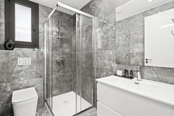Une salle de bain moderne avec une douche à parois de verre, un meuble-lavabo blanc et des murs en marbre.