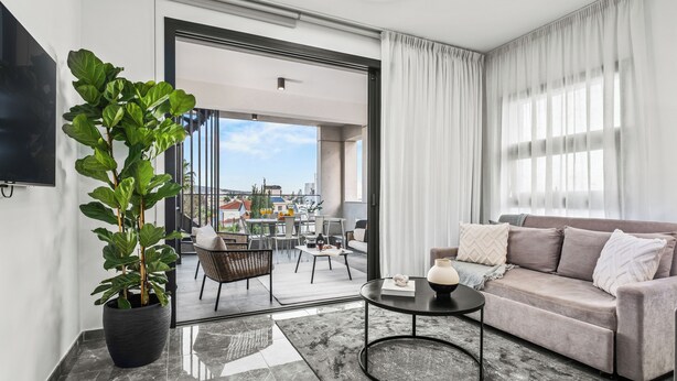 A modern living room with a sofa, a coffee table, and a potted plant. - Noir Luxury Residence - Rooftop & Jacuzzi by Nomads (Limassol)