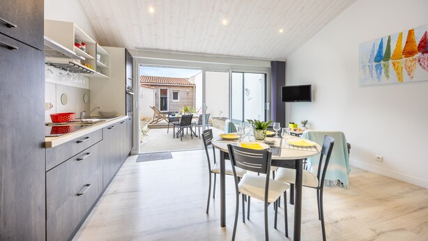 Cocina moderna con comedor, televisor montado en la pared y vistas al exterior.