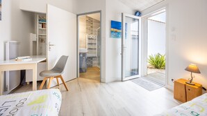 Un dormitorio con cama, escritorio, silla, armario y puerta que da a un balcón.