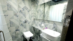 A bathroom with a white toilet, a white sink, and a mirror above the sink. The walls are tiled with a geometric pattern. - Host Inn Mumbai Airport (Mumbai)