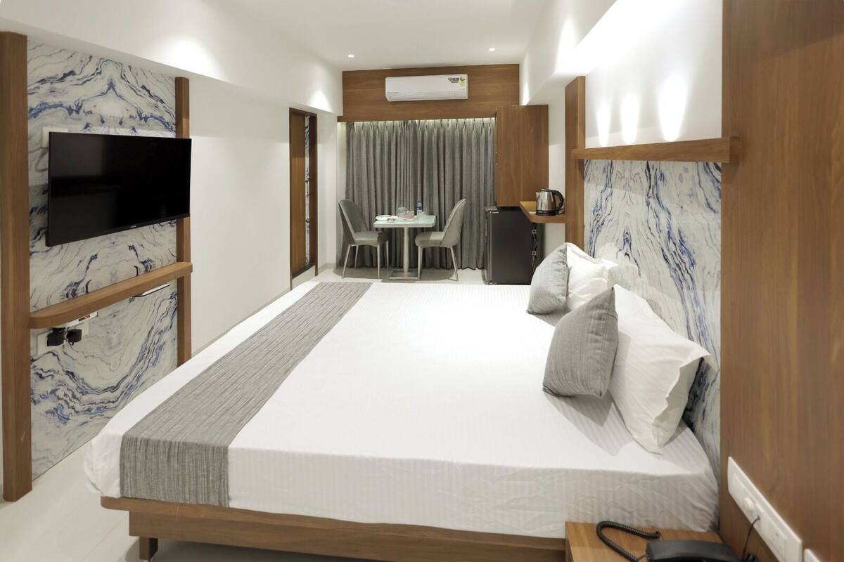 A modern hotel room with a large bed, a TV, a dining area, and a bathroom.