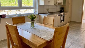 A kitchen with wooden cabinets, a dining table with chairs, a vase with flowers, and a window with curtains. - Apartment 'Am Weinberg' with Garden, Balcony and Wi-Fi (Oberkirch)