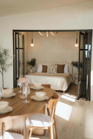 A modern bedroom with a large bed, bedside tables, and a dining area with a wooden table and chairs. - Kasa Dharma an oceanfront House (Ensenada)