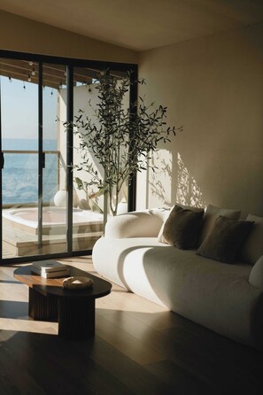 Sala de estar moderna com sofá, mesa de centro e uma janela grande com vista para uma varanda e o mar.