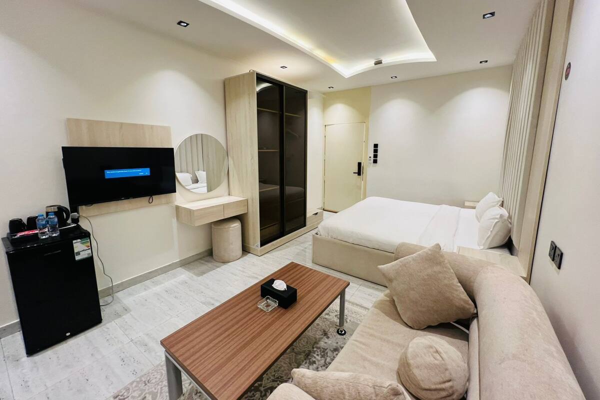 A modern hotel room with a bed, a TV, a desk, a sofa, and a coffee table.