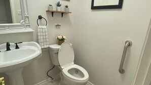 A bathroom with a white sink, toilet, and a small shelf with plants. - La Casa De Francella (Harris County)