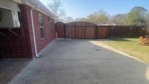 A residential backyard with a concrete driveway, a wooden gate, and a brick house. - La Casa De Francella (Harris County)