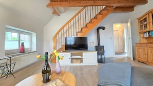 A living room with a wooden staircase, a television, a fireplace, and a bookshelf. - Ferienhaus Strandkrabbe - Comfortable vacation home Strandkrabbe with large garden (Neßmersiel)