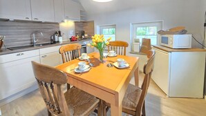 A modern kitchen with wooden cabinets, a dining table with chairs, a coffee station, and a microwave. - Ferienhaus Strandkrabbe - Comfortable vacation home Strandkrabbe with large garden (Neßmersiel)
