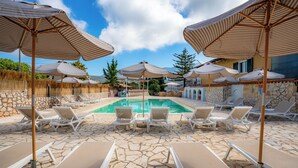 Un área junto a la piscina con sillones de descanso y sombrillas a rayas.