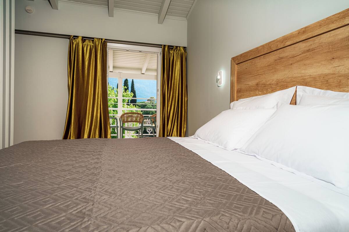 A hotel room with a large bed, a wooden headboard, a balcony with a view, and a window with curtains.