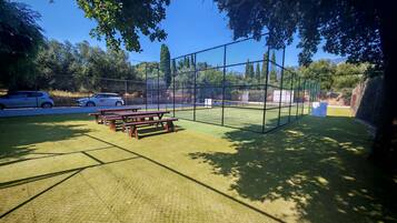 Un court de tennis avec un filet, entouré d’une clôture, et des tables de pique-nique au premier plan.