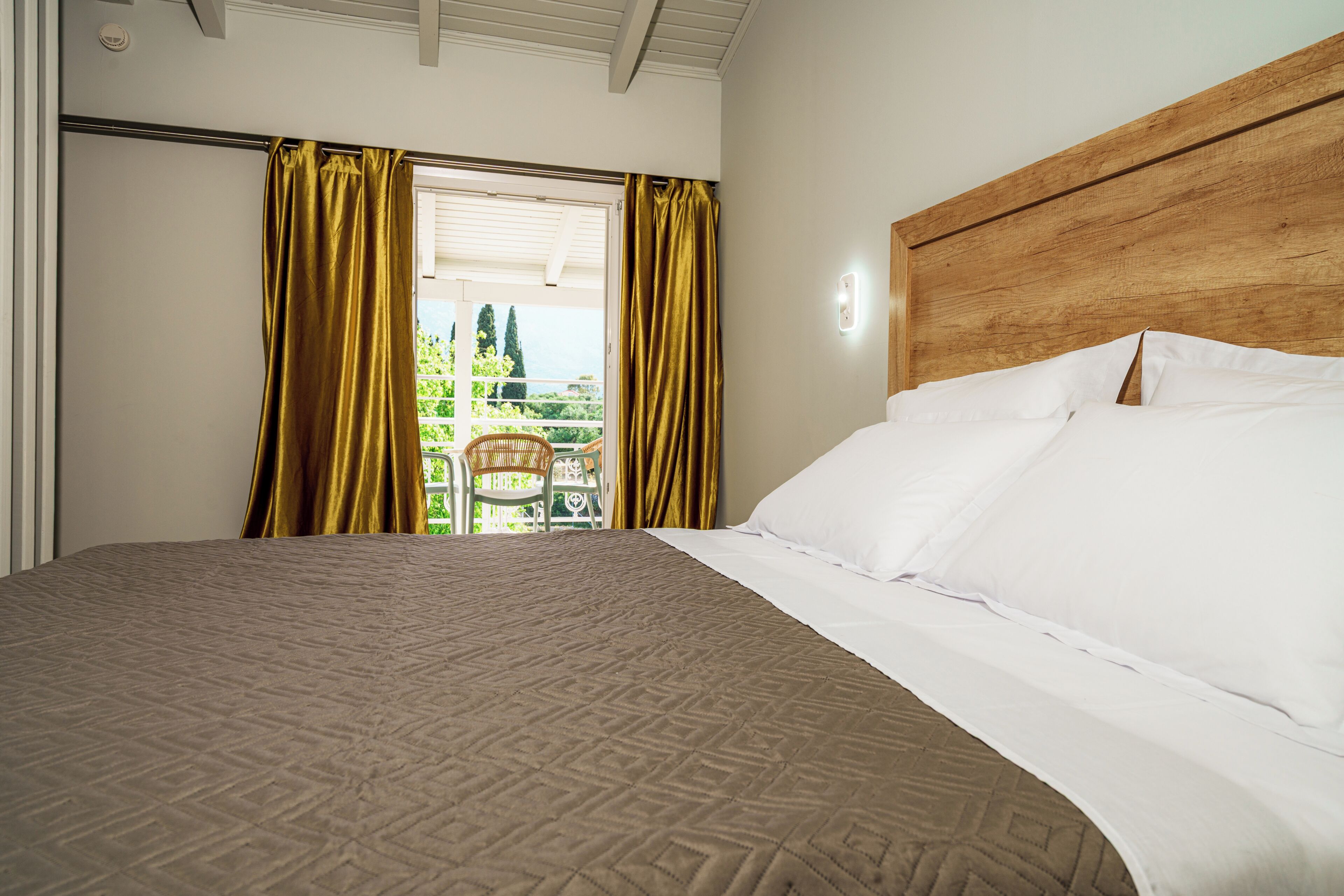 A hotel room with a large bed, a wooden headboard, and a view of a balcony with chairs.