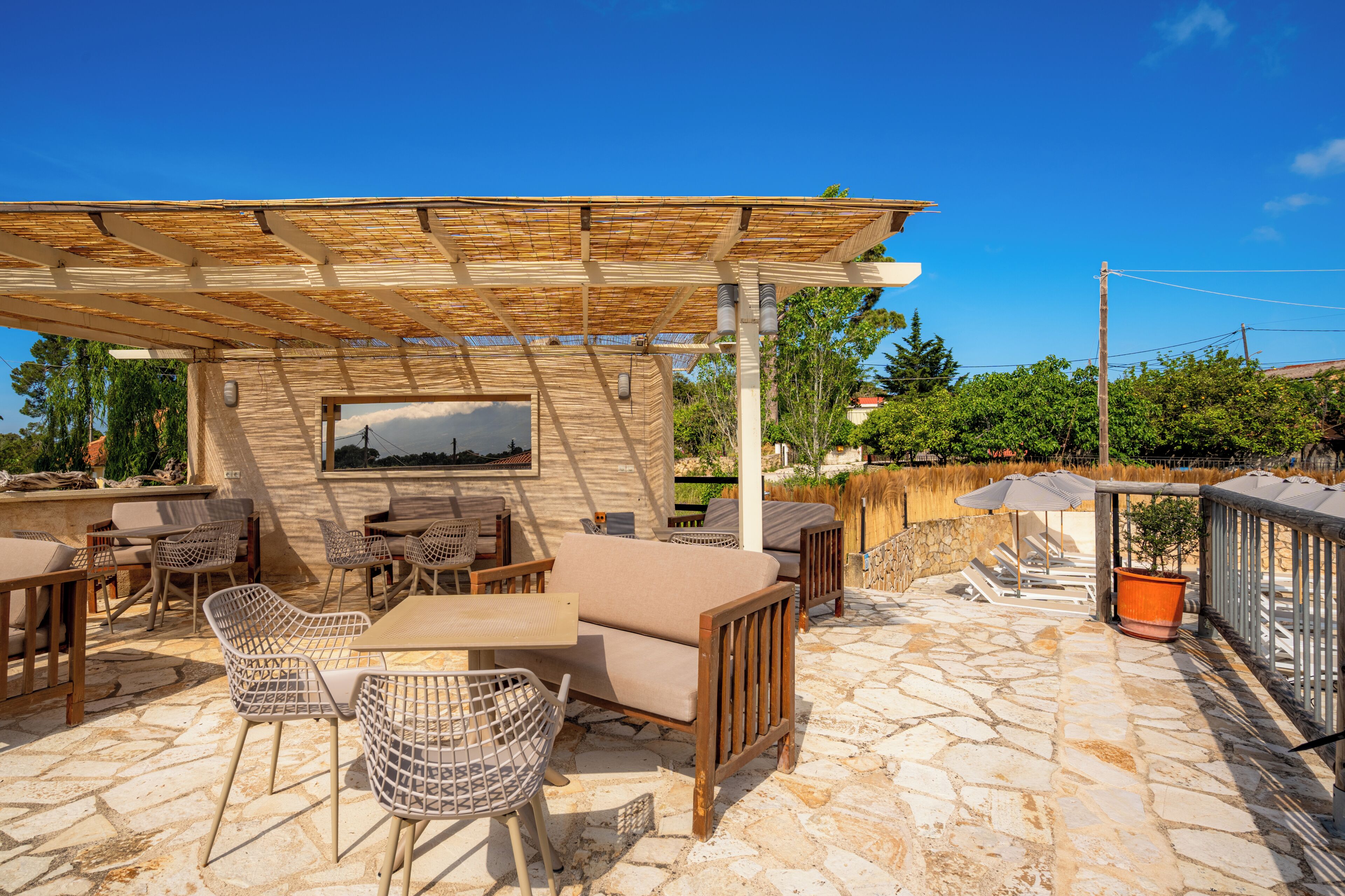 Un patio exterior con suelo de piedra, mobiliario de madera y una estructura de pérgola.