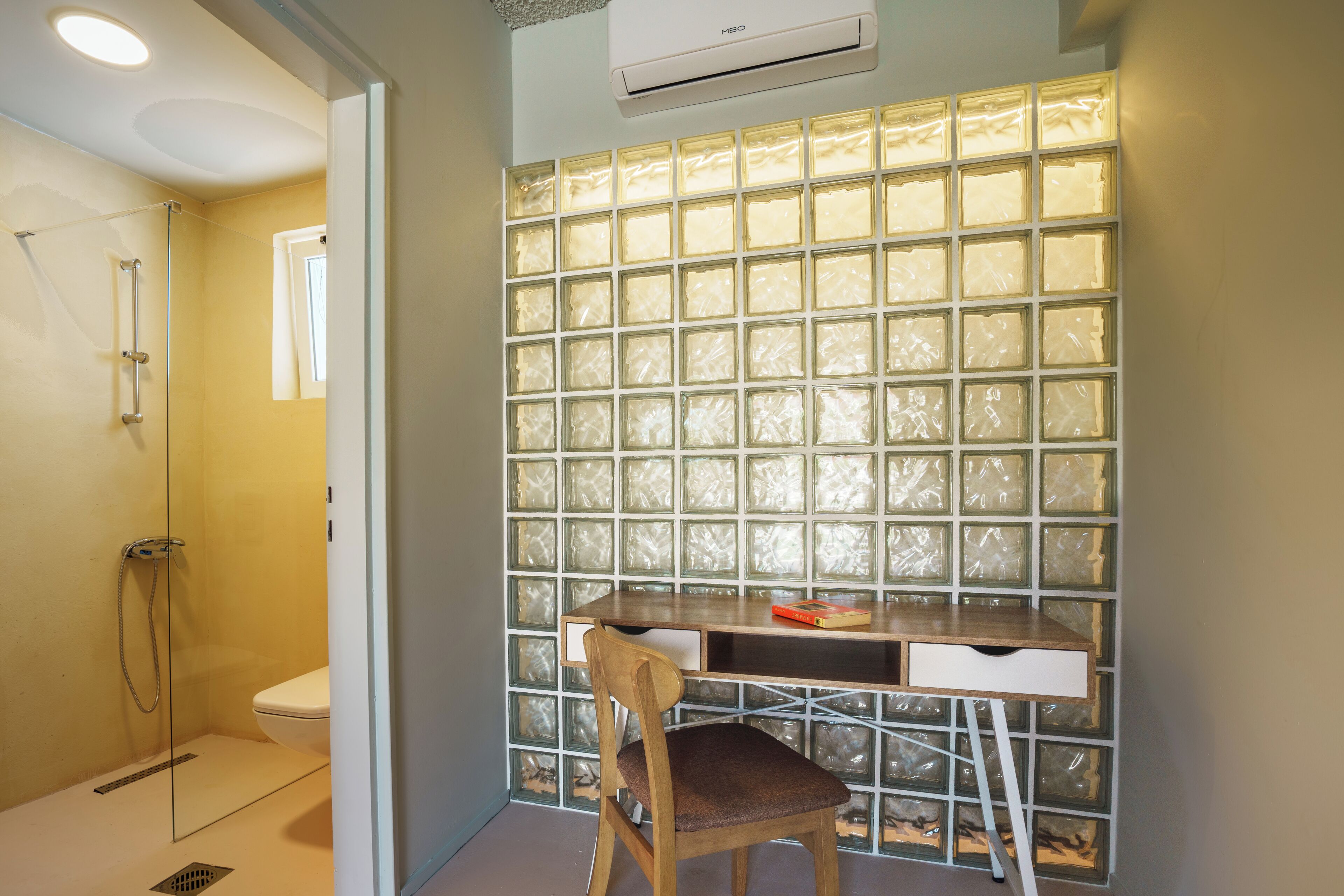 Baño con ducha, inodoro, escritorio y silla, y panel de vidrio esmerilado en la pared.