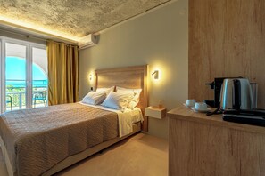 A hotel room with a bed, a small bedside table with a coffee maker, and a view of the outdoors. - Coudour Boutique Hotel (Kefalonia)