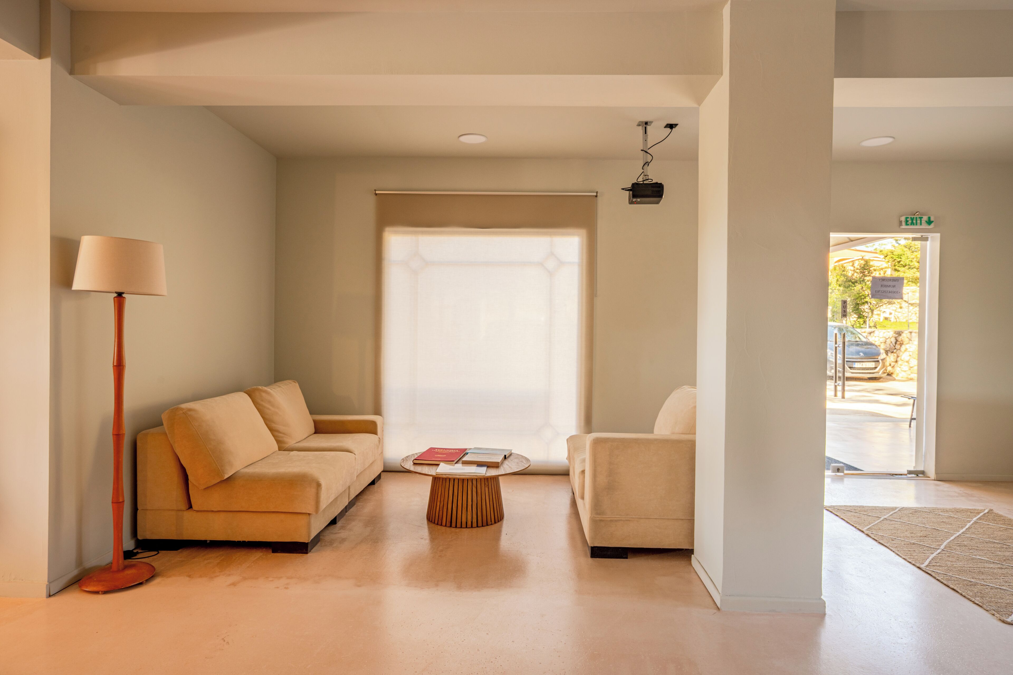 A modern hotel room with a sofa, armchair, floor lamp, and a small table.