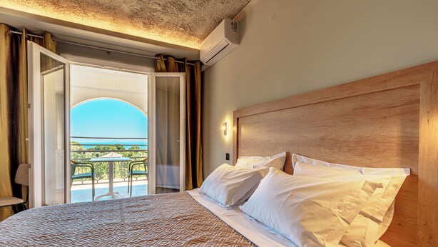 Habitación de hotel con una cama grande, cabecera de madera y balcón con vistas al mar.